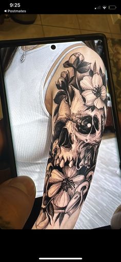 a person holding up a cell phone with a skull and flowers tattoo on their arm