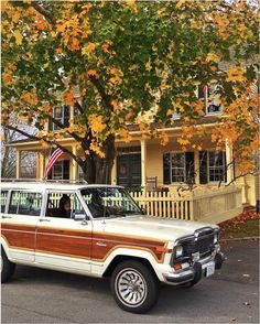 an old station wagon parked in front of a house with autumn leaves on the trees