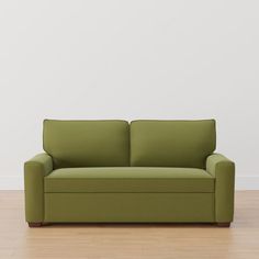 a green couch sitting on top of a hard wood floor next to a white wall