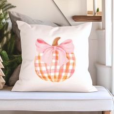 a white pillow with a pink bow sitting on top of a chair next to a christmas tree