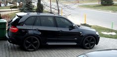 a black car parked on the side of a road next to a green trash can