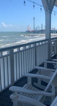 two white chairs sitting on top of a wooden deck next to the ocean and ferris wheel