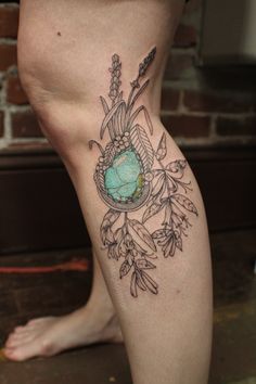 a woman's legs with tattoos on them and flowers in the center, along with a turquoise stone