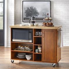 a microwave is on top of a small wooden cart with dishes and cups in front of it