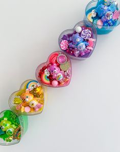 four heart shaped boxes filled with different types of candies on a white table top