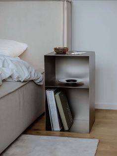 a book shelf in the corner of a bedroom next to a bed with white sheets