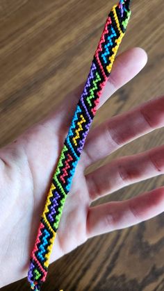 a hand holding a colorful bracelet on top of a wooden table next to a string