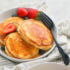 pancakes with strawberries and blueberries in a white bowl on a striped tablecloth