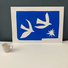 a blue and white card with two birds on it next to a coffee cup in the foreground