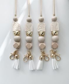 four white and gold beaded necklaces hanging from hooks with tassels on them