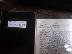 an open notebook sitting on top of a wooden table next to a cell phone and keyboard