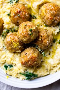 some meatballs are sitting on top of mashed potatoes and garnished with herbs