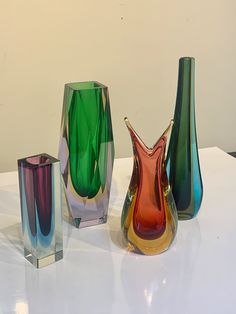 three colorful vases sitting on top of a white table next to eachother