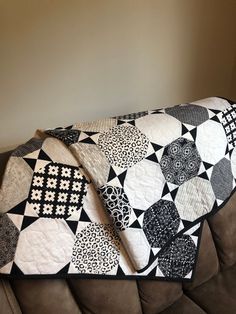 a black and white patchwork quilt sitting on top of a brown couch next to a wall