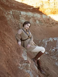 a woman is leaning against the side of a cliff while wearing boots and a dress