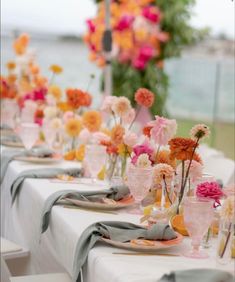 the table is set with many different colored flowers in vases and glassware on it