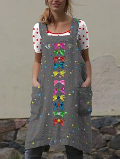 a woman standing in front of a stone wall wearing a dress with colorful designs on it