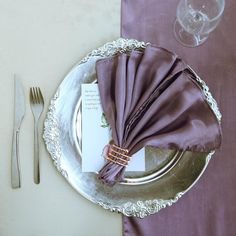 a place setting with purple napkins and silver plates