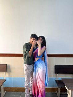 a man standing next to a woman in a pink and blue sari on top of a bench