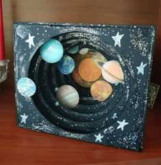 the solar system is made out of cardboard and painted with paint on it, sitting on a table next to a red candle