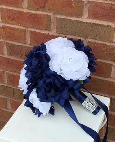 a bridal bouquet with blue and white flowers on a table in front of a brick wall