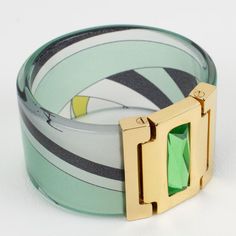 Lovely chunky Emilio Pucci gilded metal, acrylic, and silk bracelet bangle. Large bangle shape of a clear acrylic band with multicolor Pucci silk inclusion. The bracelet is also ornate with a gilt metal faux hinge topped with a huge rectangular faceted resin rhinestone. Assorted colors of emerald green, avocado green, black, and white. Emilio Pucci's hallmark is engraved on the inside and reads "Emilio Pucci - Made in Italy". Comes with its original branded gift box. Measurements: inside across Lucite Bangle Bracelet As Gift, Lucite Bangle Bracelet For Gift, Lucite Bangle Bracelets As Gift, Modern Lucite Bangle Jewelry, Designer Green Bracelets As Gift, Designer Green Bracelets For Gifts, Modern Lucite Bracelets As A Gift, Elegant Green Bracelets, Green Avocado