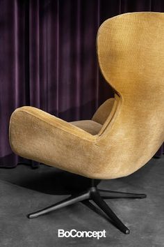 an upholstered chair sits in front of a purple curtain