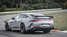 the rear end of a silver sports car driving on a road with trees in the background