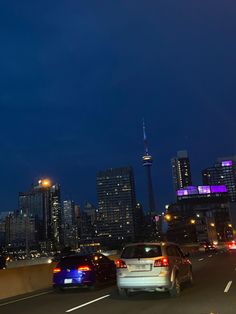 cars are driving down the highway in front of some tall buildings at night with lights on