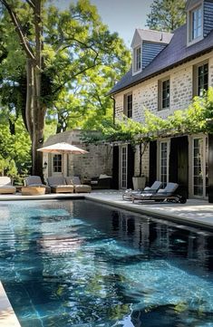 an outdoor swimming pool with lounge chairs and umbrella in front of a large stone house