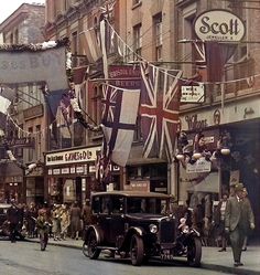 an old photo of people walking down the street in front of buildings with flags on them