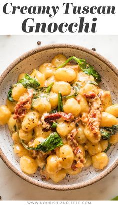 a bowl filled with pasta and spinach on top of a white table next to a green leaf