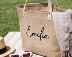 a personalized tote bag sitting on top of a blanket next to sunglasses and a hat