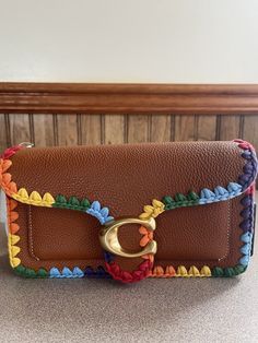 a brown leather purse with multicolored crochet trimmings and a gold buckle