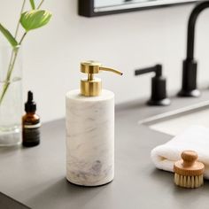 a white marble soap dispenser sitting on top of a counter next to a brush