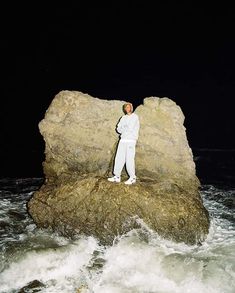 a man standing on top of a rock next to the ocean