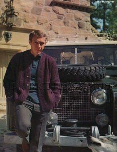 an older man sitting on the hood of a car in front of a stone building