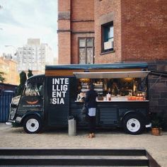 a black food truck parked in front of a brick building with people standing around it