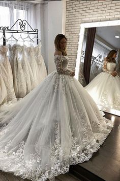 a woman standing in front of a mirror wearing a white wedding dress with long sleeves