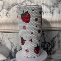 a white vase with red strawberries on it sitting on top of a marble counter