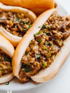 three hot dogs on buns covered in chili and relish sitting on a plate