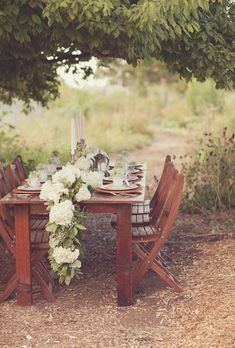 a wooden table with white flowers on it under a tree