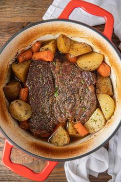 a pot filled with meat, potatoes and carrots on top of a wooden table