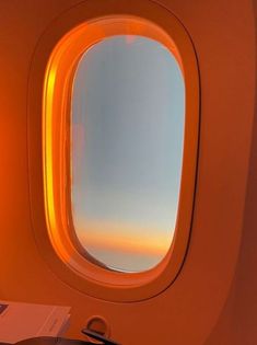 an airplane window looking out at the sky and clouds from inside, with a book on the table beside it