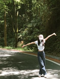 a woman in white shirt and jeans skateboarding on paved area next to wooded area