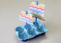 an egg carton with two paper boats in it and one boat on the top