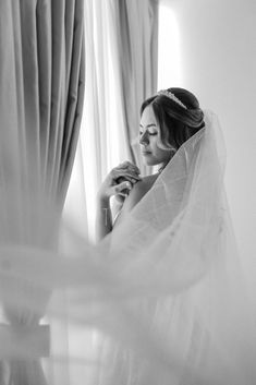 a woman in a wedding dress looking out the window with her veil draped over her head