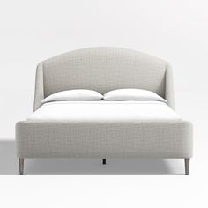 an upholstered bed with white sheets and pillows