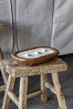 three candles are placed in a wooden tray on a stool