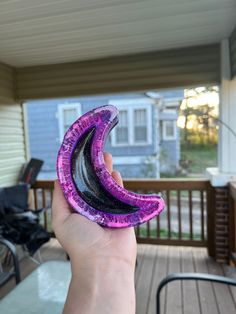 a person holding up a purple and black object in front of a porch with chairs